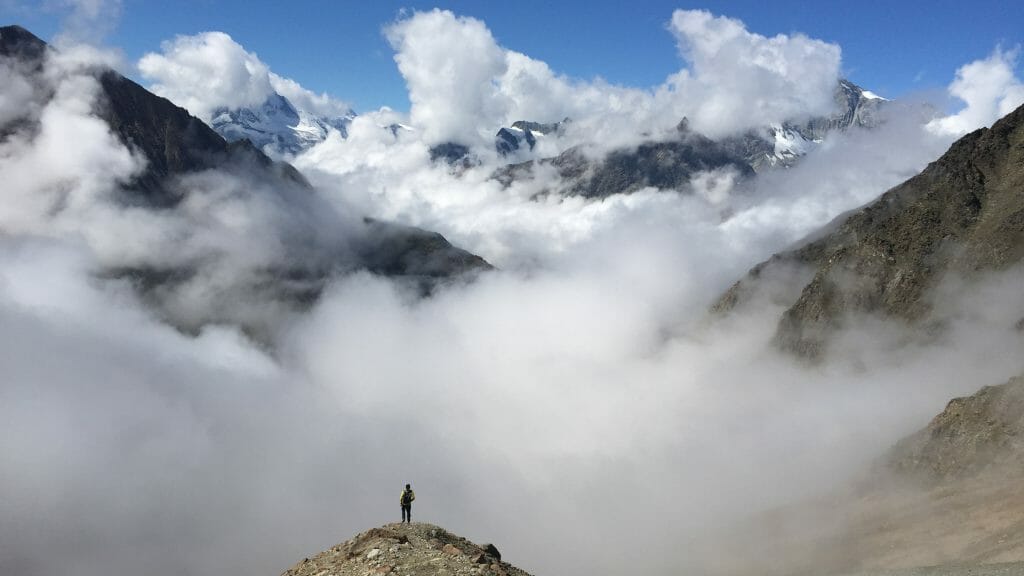 Climber on top of a rocky mountain in Switzerland, looking at massive clouds and mountains in the background