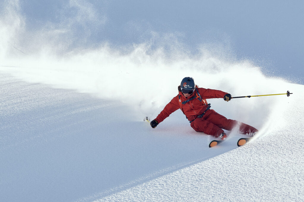 Woman in red snow suit and helmet skiing deep powder.