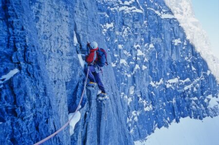 a climber scales an icy blue vertical rock