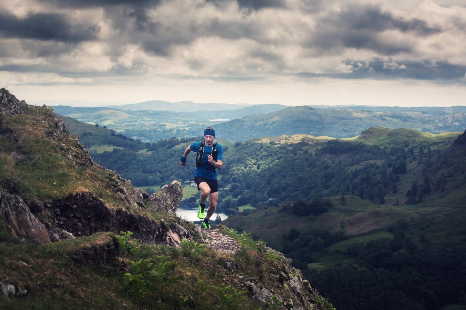 Trail runner Damian Hall running along the side of a mountain with vast mountain landscape in the background