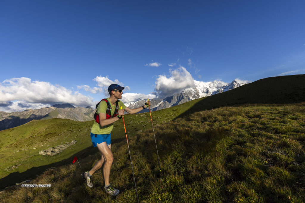 A male runner hiking uphill with poles in both his hands.