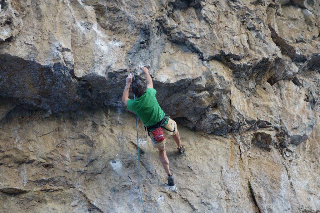 A rock climber on a wall wearing a green t-shirt.