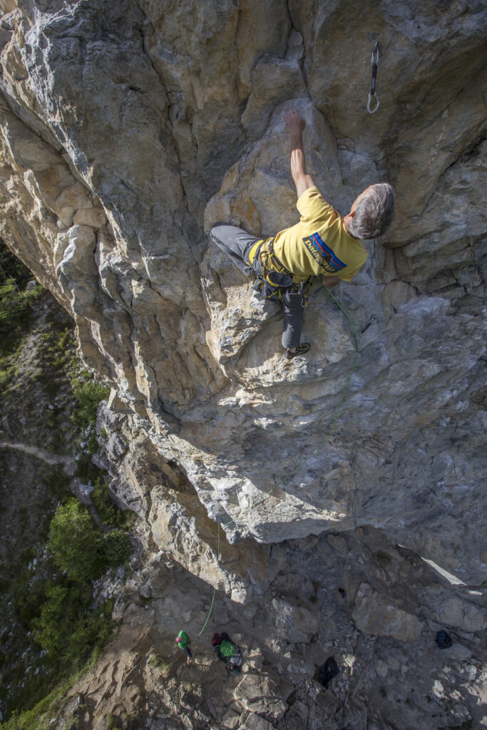 A climber in a yellow Patagonia t-shirt on a slight overhang.