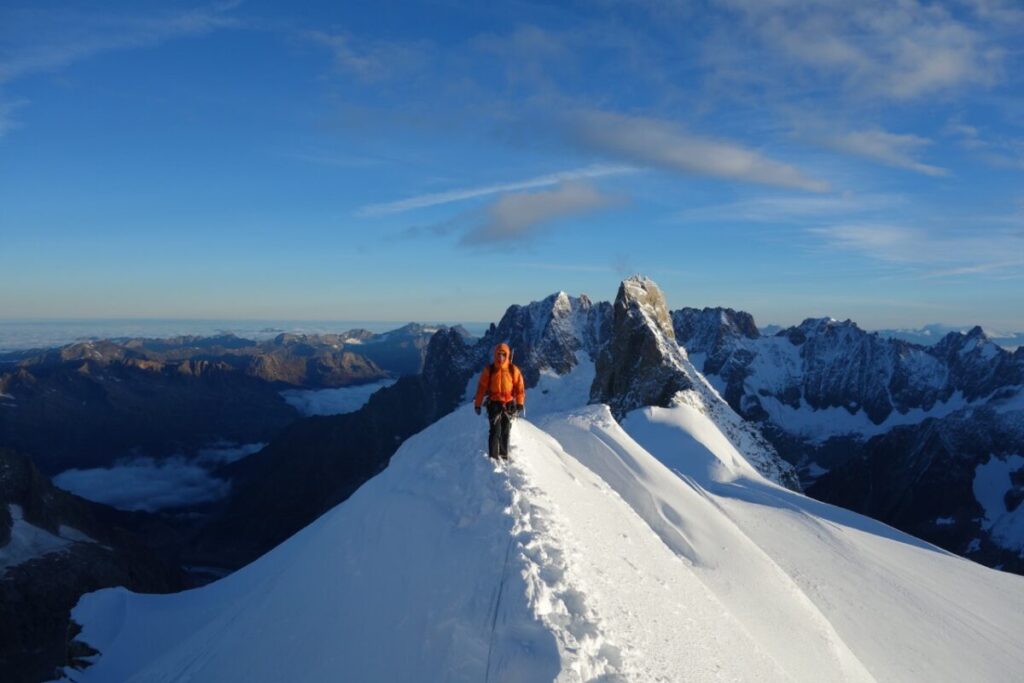 Understanding Training Essentials for Mountaineering: A Podcast Series A person in an orange jacket walking on a snow ridge.