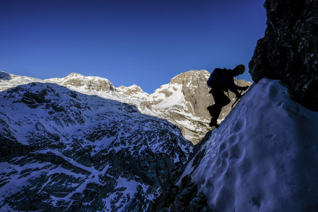 A person in silhouette climbs ice using ice axes and crampons.