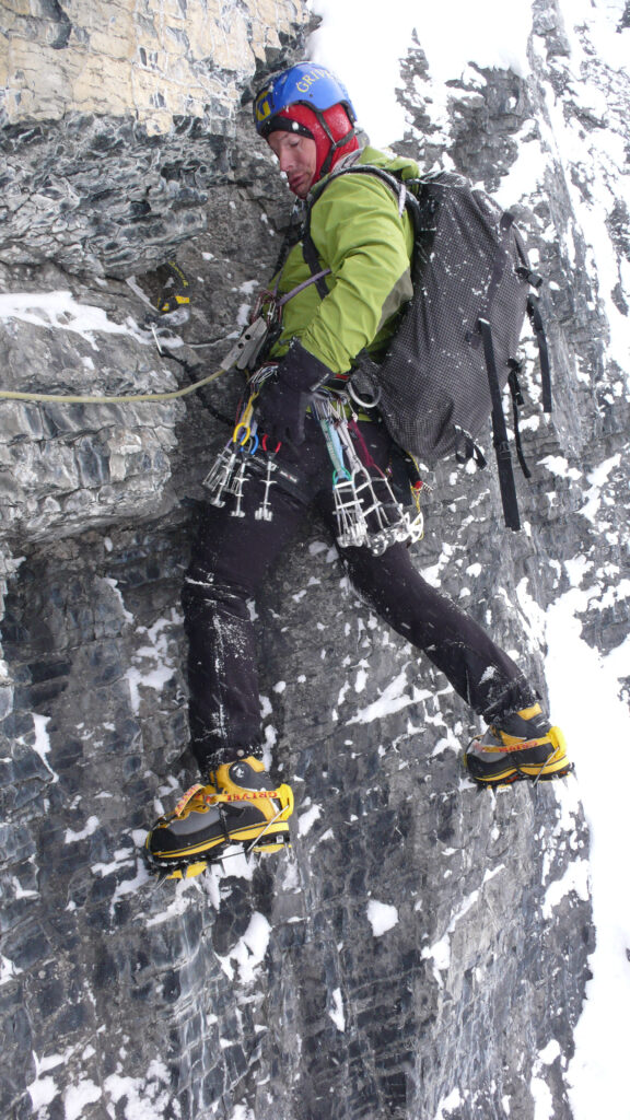 A climber hanging on a wall in snow and icy conditions with a rucksack on his shoulders.