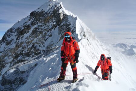 Two mountaineers in red mountaineering gear standing near a mountain summit.