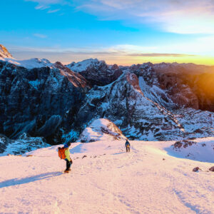 Two athletes on a downhill mountain slope at sunset.