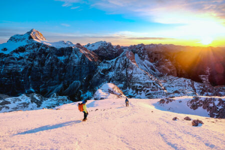 Two athletes on a downhill mountain slope at sunset.