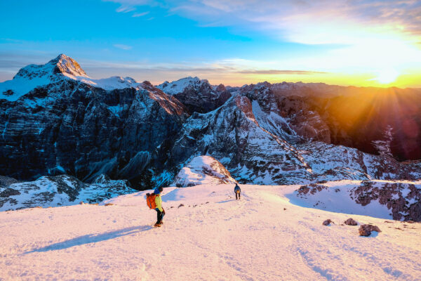 Two athletes on a downhill mountain slope at sunset.